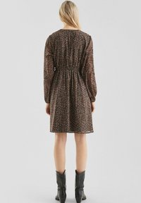 Schwarzes Blumenkleid mit langen Ärmeln, geraffter Taille und ausgestelltem Rock. Weiches Material und dezentes Muster; getragen mit schwarzen Cowboy-Stiefeln.