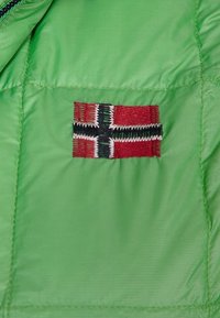 Interiér zelené bundy s malou vyšívanou norskou vlajkou s červenými, černými a bílými detaily na hladké tkanině.