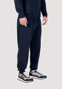Marineblaue Jogginghosen aus weichem Stoff, mit einem elastischen Bund und Bündchen an den Knöcheln. Kombiniert mit grauen und marineblauen Sportschuhen.