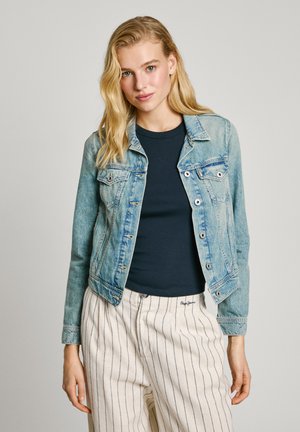 Light blue denim jacket with four front pockets, silver buttons, and a slightly faded texture, worn over a dark blue shirt and striped pants.