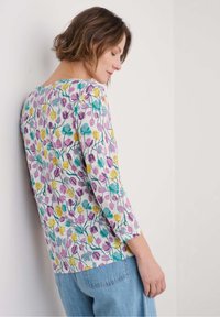 Top a maniche lunghe floreale con scollatura rotonda, caratterizzato da un motivo di fiori multicolori in viola, giallo e verde acqua su uno sfondo bianco.