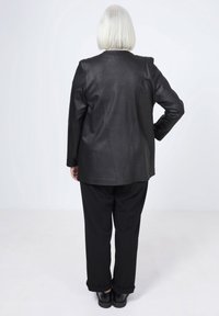 Veste en cuir noir avec une finition texturée, dotée d'une coupe ajustée et d'un design à dos droit, associée à un pantalon noir ample.