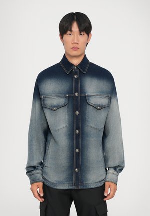 Jeansjacke mit einem verblassten Farbverlauf von dunkelblau oben zu hellblau unten, mit zwei Brusttaschen und silbernen Knöpfen.