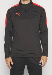 Schwarzer sportlicher Pullover mit roten Schulterakzenten, Reißverschluss am Kragen und orangefarbenem Logo. Glatter Stoff mit langen Ärmeln und figurbetontem Schnitt.