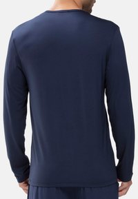 Mężczyzna w jednolitej granatowej koszuli z długim rękawem, pokazany od tyłu na białym tle.