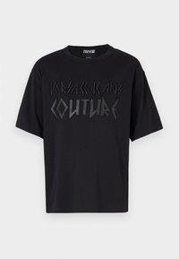 Melna, pārkāpjama T-krekls, izgatavots no kokvilnas, ar strukturētu melnu logo "VERSACE JEANS COUTURE" izteiksmīgā, leņķiskā fontā uz krūtīm.