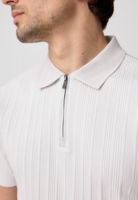 Light gray collared polo shirt with textured fabric, vertical stripes, and a half zipper. Features a ribbed collar and short sleeves.