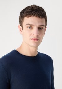 Sötétkék pulóver, kerek nyakkivágással, puha anyagból készült. Hosszú ujjakkal és sima textúrával rendelkezik. Egyszerű, minta nélküli dizájn.