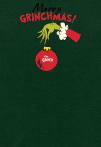 Maglione di Natale verde con un ornamento rosso con la scritta "The Grinch" e una mano del Grinch che lo tiene. Testo "Buon Grinch Natale!" sopra.