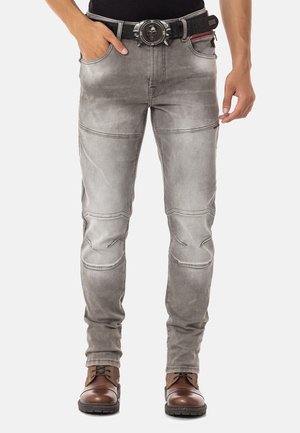 Graue Motorradjeans mit einer enganliegenden Passform, sichtbaren Nähten, strukturiertem Material und Kniepaneelen. Kombiniert mit braunen Stiefeln.