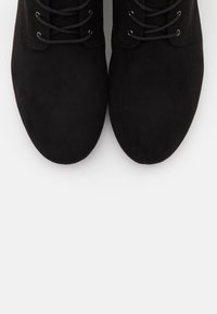 Le scarpe in suede nere presentano una punta arrotondata e un design con lacci, dotate di lacci e occhielli neri. La texture è liscia con una finitura opaca.