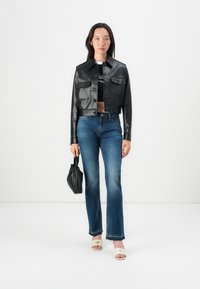 Sort skinnjakke i lær med frontlommer, kombinert med blå vide jeans og hvite åpen-tå sandaler. Svart mini-veske i hånden.