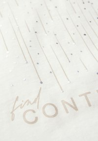 Bílá látka s metalickými flitry a tištěnými linkami. Text "najděte OVLÁDÁNÍ" je částečně viditelný v světlé béžové barvě.