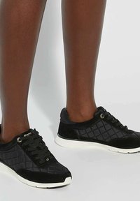 Black quilted sneakers featuring a combination of fabric and suede, with round laces and white rubber soles. Gold accents present on the side.