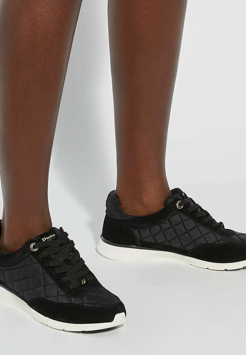 Black quilted sneakers featuring a combination of fabric and suede, with round laces and white rubber soles. Gold accents present on the side.