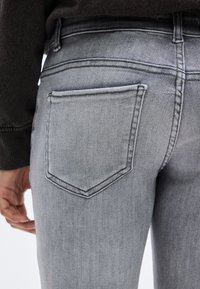 Γκρι τζιν παντελόνι με denim ύφασμα, σε οπίσθια γωνιακή όψη, με μία πλαϊνή τσέπη και ορατά ραψίματα, παρουσιάζοντας μια ομαλή, ελαφρώς ξεθωριασμένη υφή.