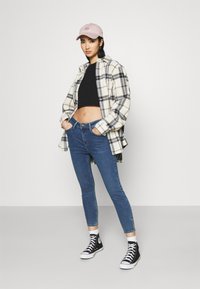 Conjunto informal que incluye una camiseta negra corta, una camisa de franela a cuadros en crema y negro, jeans ajustados azules y zapatillas altas negras. Gorro rosa.
