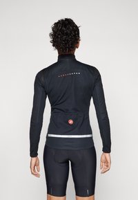 Black long-sleeve cycling jersey with a high collar, reflective accents, and a rear pocket. Features a fitted design and soft texture.