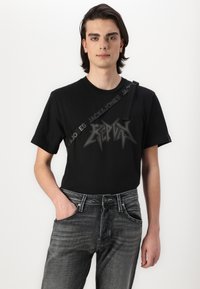 Zwarte T-shirt met korte mouwen met een opvallend grafisch logo in grijs. Gecombineerd met strakke donkergrijze spijkerbroek met een lichte vervaging en zichtbare zakken.