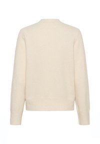 Pull crème en tissu doux, avec un col rond, des manches longues et un ourlet côtelé. Texture lisse sans motifs visibles.