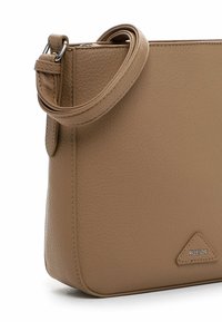 Beige Leder Umhängetasche mit strukturierter Oberfläche, ausgestattet mit einem abgerundeten Schulterriemen und einem silbernen Logo-Anhänger in Dreiecksform.