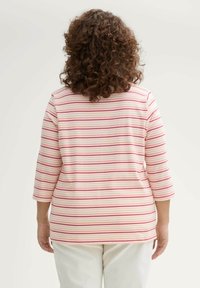 Top a righe con design rosa e bianco, realizzato in tessuto morbido, con maniche a tre quarti e una vestibilità rilassata. Pantaloni bianchi indossati sotto.
