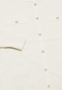 Cardigan bianco testurizzato con due tasche frontali, piccoli bottoni rotondi e polsini a costine; presenta un motivo intrecciato e un tessuto morbido.
