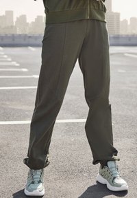 Olijfgroene sweatpants met een getailleerd design, zachte stof en naaddetails; gecombineerd met lichtgroene en witte sneakers.