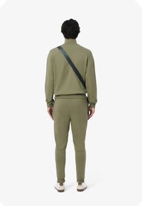 Olijfgroen trainingspak met een hoge kraag, voorzien van een zwarte diagonale band. Slank model, zachte stoftextuur en elastische enkels.