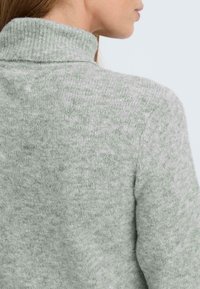 Hellgrauer Rollkragenpullover mit einem strukturierten Strickmuster. Der Stoff wirkt weich und warm und weist ein enganliegendes Design mit einem gerippten Kragen auf.
