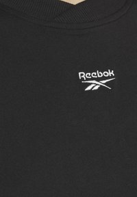 Svart crew-neck sweatshirt i en slät tyg med en vit broderad Reebok-logotyp på bröstet. Inga mönster eller ytterligare detaljer synliga.