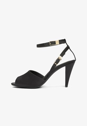 Black high-heeled open-toe sandal with two gold buckle ankle straps and a tapered heel on a white background.