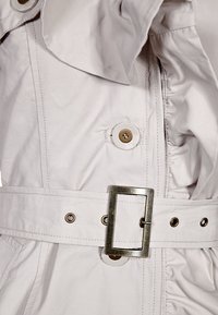 Lichtbeige trenchcoat met een gerimpelde kraag, knoopdetails en een brede riem met een rechthoekige metalen gesp en bijpassende knoopaccenten.