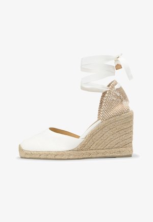 Sandale compensée blanche en espadrille avec semelle en jute tressée, bout fermé, talon tissé et liens à nouer autour de la cheville.