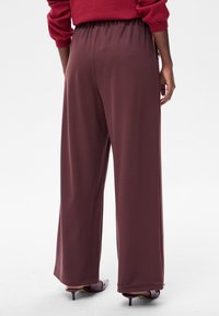 Spodnie o szerokich nogawkach z głębokiego bordowego materiału. Posiadają elastyczną talię i gładką fakturę. Połączone ze szpiczastymi szpilkami.