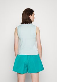 Top sem mangas azul claro feito de tecido texturizado, com um decote redondo. Combinado com calções em teal de corte largo e com bolsos laterais.