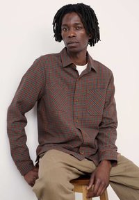 Knoop-up geruit overhemd in bruin-, groen- en blauwtinten, met twee borstzakken en knoopsluiting, gecombineerd met kaki broeken.