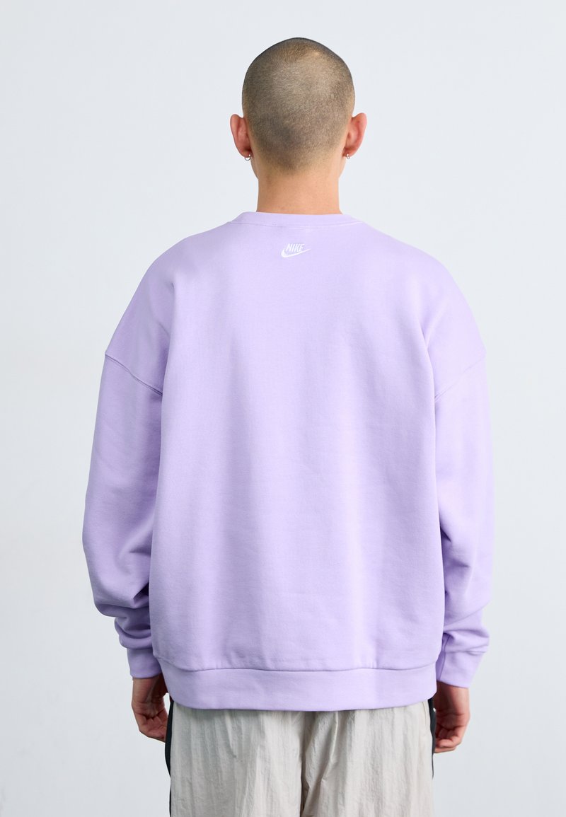 Sweatshirt oversized lavande avec un col ras du cou et des poignets côtelés. Présente un petit logo Nike blanc dans le haut du dos. Matière en coton doux.