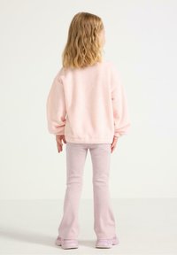 Lyserød fleece-pullover med pufærmer, parret med lyserøde flagrende bukser. Outfittet afsluttes med lyserøde sneakers.