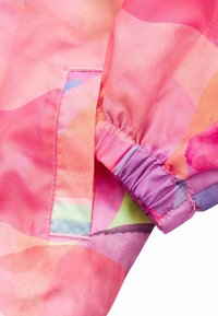 Veste rose colorée avec un motif aquarelle, des poignets élastiques et une poche latérale avec un bord contrastant en violet clair et vert.