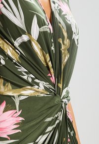 Vestito floreale verde con un dettaglio annodato in vita, decorato con motivi floreali rosa e bianchi, realizzato in un tessuto morbido e leggero.