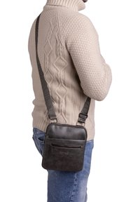 Borsa a tracolla in pelle nera con tasca frontale con zip e tracolla regolabile, caratterizzata da una superficie testurizzata e forma rettangolare.