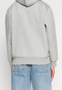 Grijze capuchontrui met een gestructureerde afwerking, voorzien van ribgebreide manchetten en een zoom, gecombineerd met lichtblauwe denim jeans.