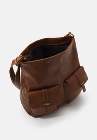 Brown leather bag with a textured surface, two front pockets, and a wide opening. Adjustable strap made of matching leather.