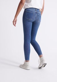 Smala jeans i mörkblå denim, med en slät yta. Har två bakfickor och en åtsittande design, parat med vita högklackade sneakers.