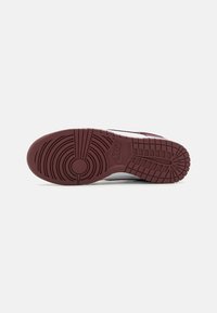 Nike sneaker outsole, featuring a maroon rubber with circular and grid patterns for traction, smooth edges, and subtle branding detail.