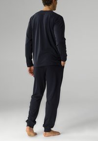 Granatowa bluzka z długim rękawem i dopasowane spodnie wykonane z miękkiego materiału, z ribbowymi mankietami i luźnym krojem. Widoczne szwy i kieszenie.