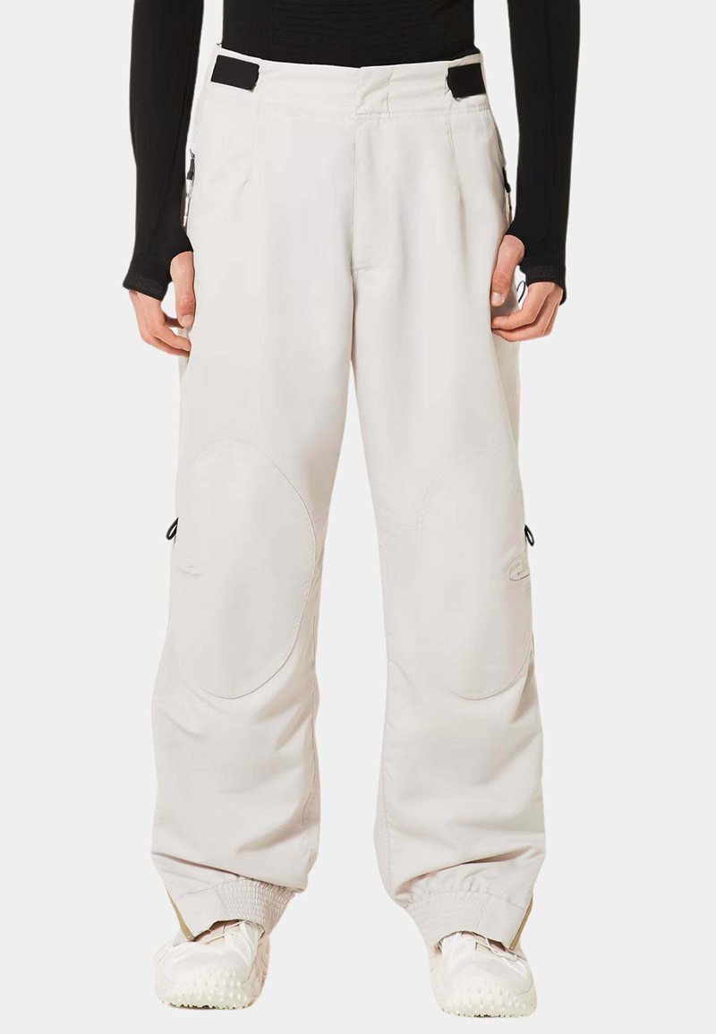 Hellgraue Schneehosen mit entspannter Passform, ausgestattet mit Knieflicken, elastischen Bündchen, Seitentaschen und schwarzen Akzenten an der Taille.