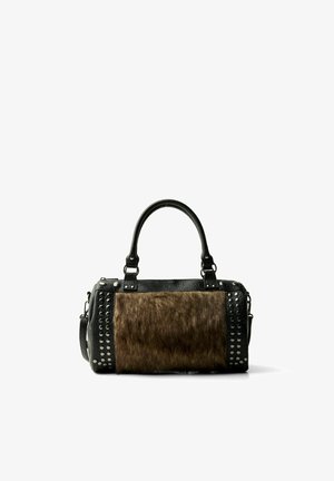 Sac à main en cuir noir avec un panneau avant en fourrure marron et des clous argentés le long des côtés et des attaches de la poignée, sur fond blanc.