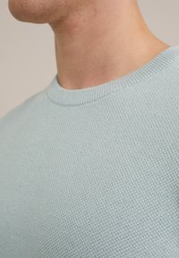 Svetlomodro teksturirano pleten pulover z okrolim izrezom, z nežnim vzorcem in rebrastimi detajli ob ovratniku.